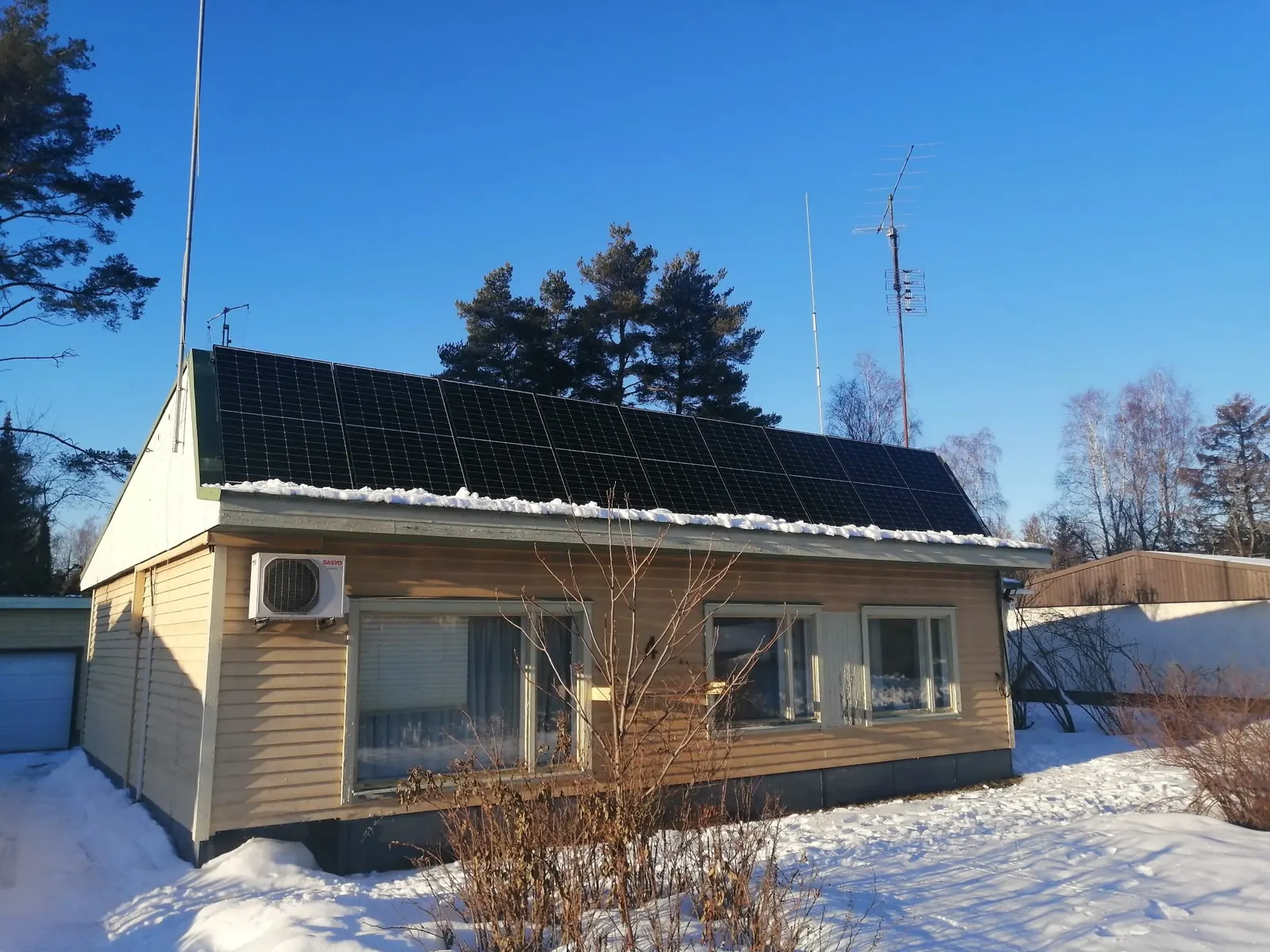 Aurinkopaneelit vaalean omakotitalon katolla lumisessa pihapiirissä
