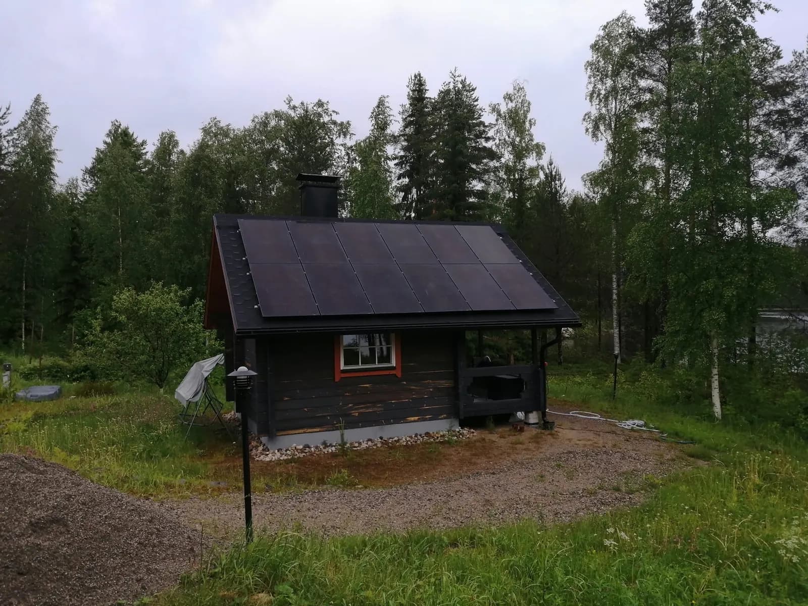 Aurinkopaneelit metsän keskellä sijaitsevan tumman hirsimökin katolla