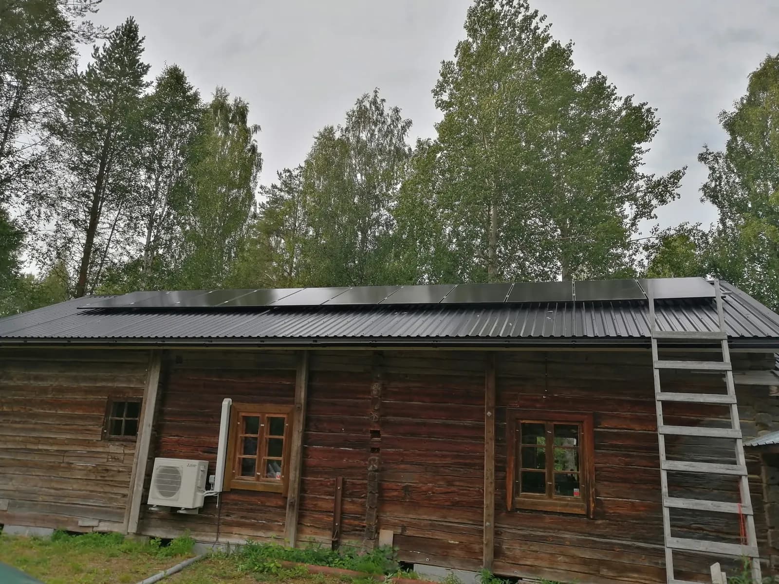 Aurinkopaneelit vanhan hirsirakennuksen peltikatolla