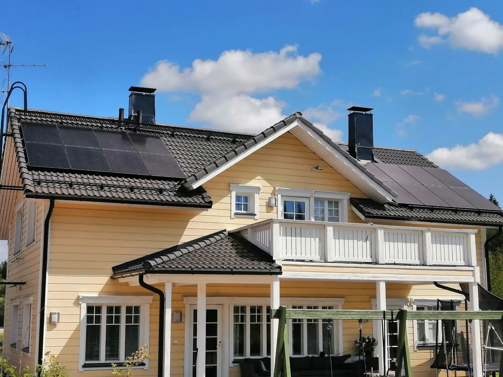 Aurinkopaneelit keltaisen kaksikerroksisen puutalon tiilikatolla